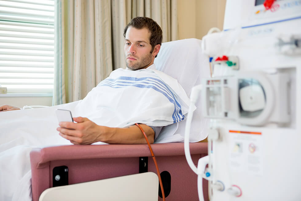 A man reads his phone while receiving hemodialysis